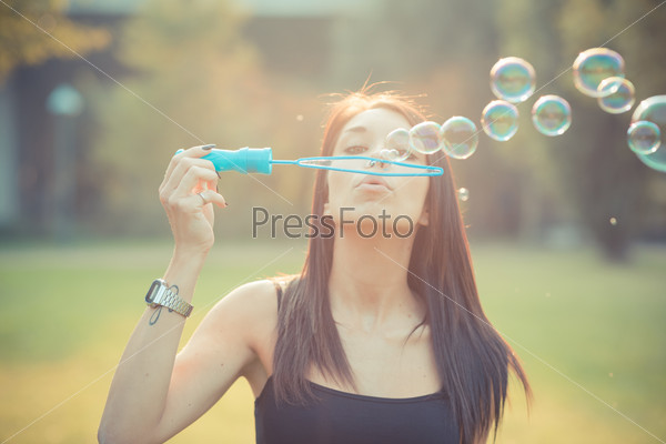 young beautiful brunette straight hair woman blowing soap bubbles outdoor