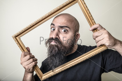 Funny bearded man with golden frame on gray background, stock photo