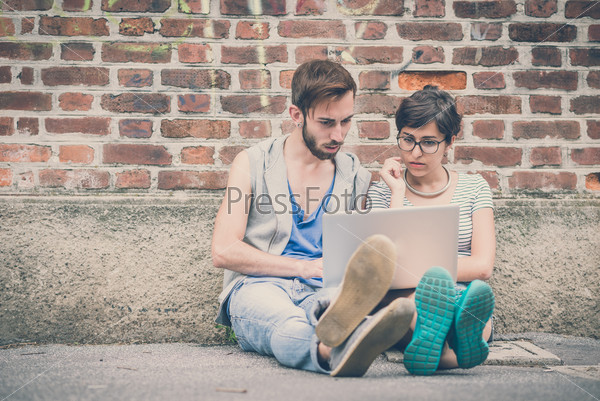 couple of friends young  man and woman using laptop in the city