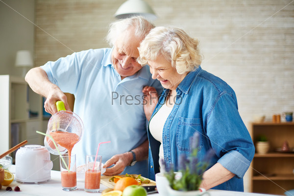Affectionate seniors making fruit smoothie in the kitchen