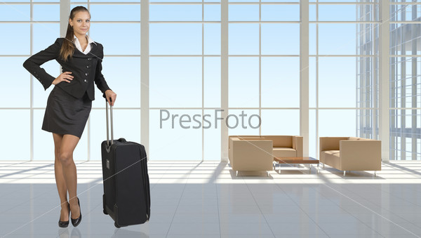 Businesswoman with travel bag in vast interior with transparent walls, looking at camera, smiling