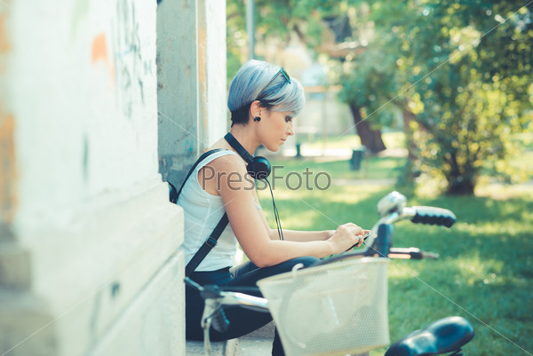 young beautiful short blue hair hipster woman with headphones music and bike in the city