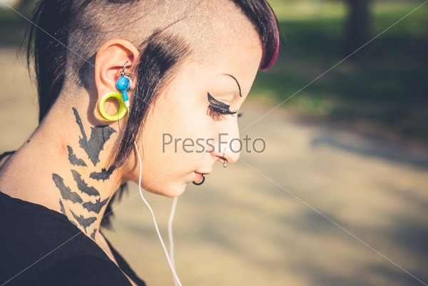 Young beautiful punk dark girl listening music in urban landscape, stock photo