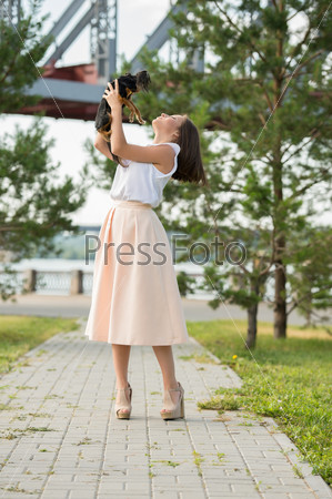 Beautiful young woman wearing elegant dress holding small dog while walking in summer park