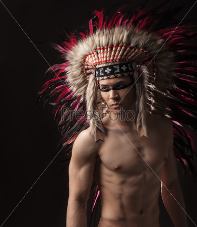 Naked indian strong man with traditional native american make up and headdress looking at the side. Close up studio shot