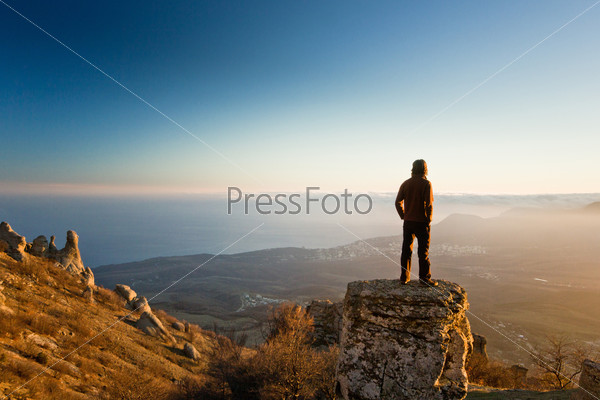 thinking man on the cliff in mountains at sunset with blue sky