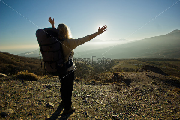 freedom girl with backpack and hands up in the mountains against sun