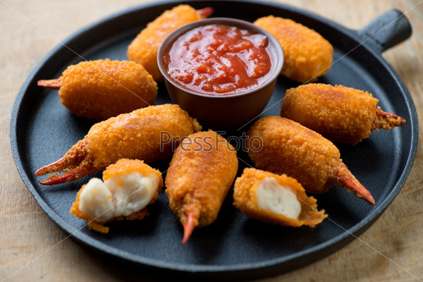 Frying pan with breaded crab claws and dip sauce, studio shot