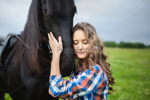 Young beautiful girl with frisian horse standing in the meadow at summer time