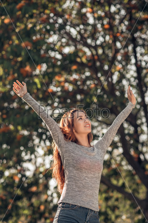 Vietnamese young woman standing in autumn park with her arms outstretched