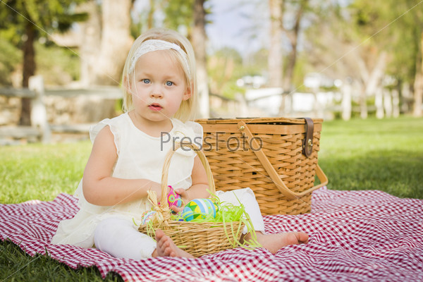 Cute Baby Girl Enjoys Enjoying Her Easter Eggs on Picnic Blanket in the Grass.