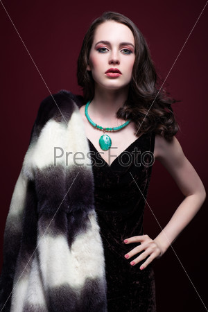 Portrait of young beautiful woman in fur coat and with green pistachio colour eyes on red marsala background
