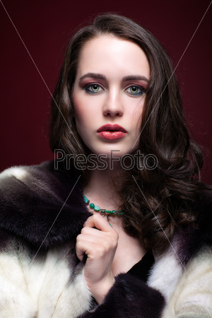 Portrait of young beautiful woman in fur coat and with green pistachio colour eyes on red marsala background