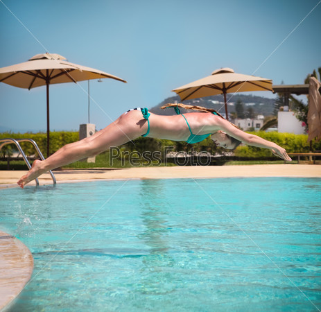 Girl jumping from a board of a swimming pool to the water. Summer fun and sport concept
