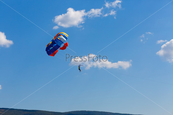 Parachutist on colorful parachute in a clear blue sky with a few clouds.