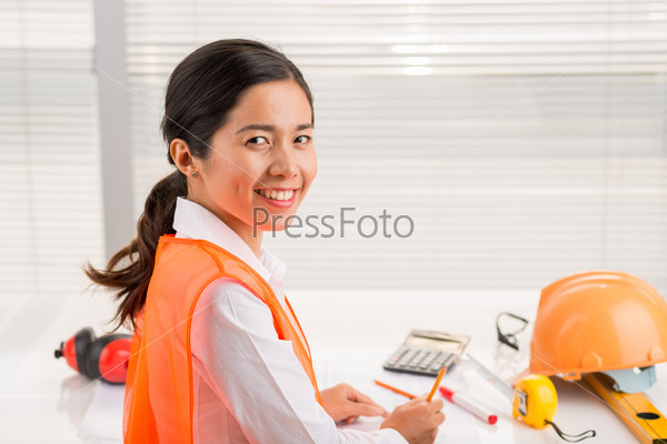 Portrait of pretty female engineer at her workplace smiling and looking at the camera