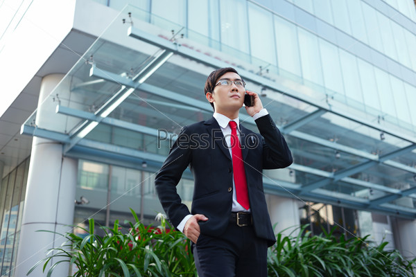 Handsome Vietnamese businessman calling on the phone outside the office building