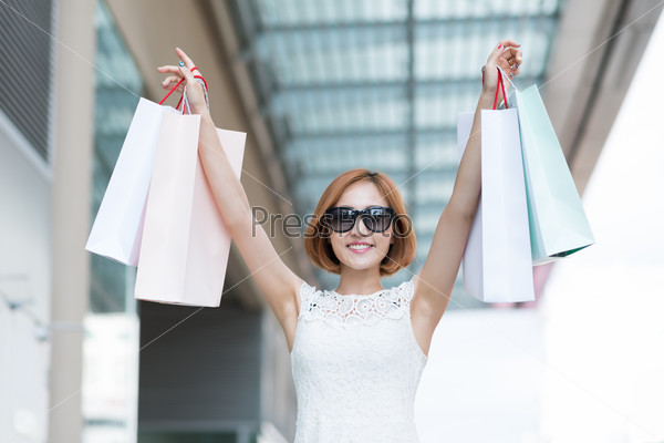 Portrait of pretty young woman raising hands with shopping bags