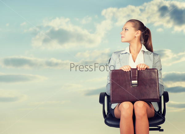 Business woman in skirt, blouse and jacket, sitting on chair and holding briefcase. Against background of sky and clouds