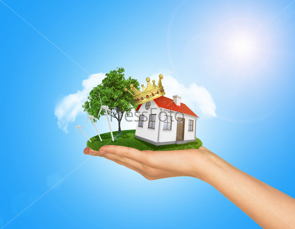 White house in hand for sale with red roof, crown and chimney. Background sun shines brightly on right. Blue sky, stock photo