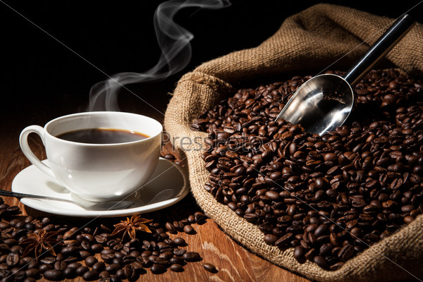 cup of coffee, coffee beans, bag on a wood table on a black background