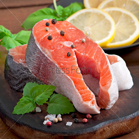Fresh and raw steaks trout on a wooden cutting board with sliced lemon, basil and pepper