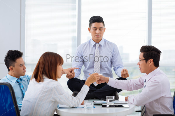 Asian business people arguing while their colleague sitting on the table in lotus position