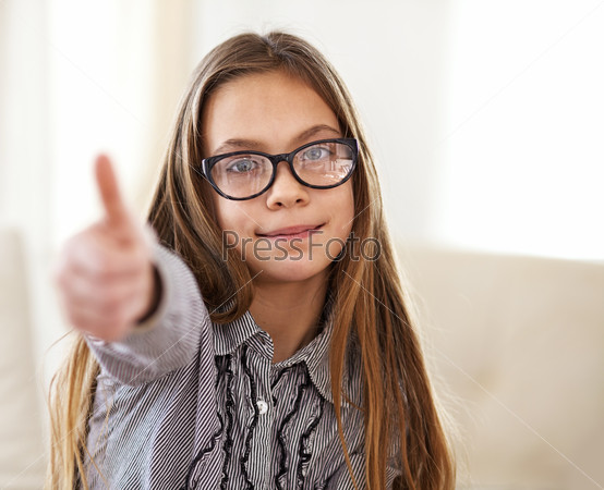 Portrait of 8 years old school girl wearing glasses looking at camera and showing thumb up