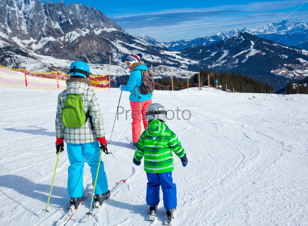 Ski, winter, snow, skiers, sun and fun - Back view of two happy kids with mother enjoying winter vacations.