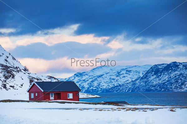 Winter in Norway - mountains with red house near the ocean.