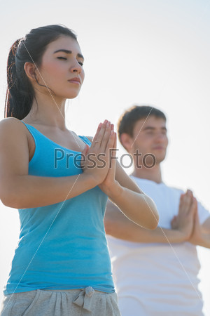 Fitness, sport, friendship and lifestyle concept - smiling couple making meditation yoga exercises on beach at morning