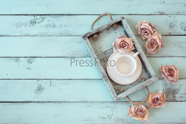 Vintage wooden tray with porcelain teacup and rose buds on shabby chic mint background, top view point