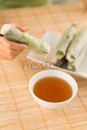 Hand holding Vietnamese spring roll above the bowl with dipping sauce