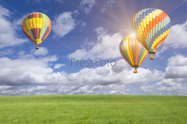 Two Hot Air Balloons Up In The Beautiful Blue Sky With Grass Field Below.