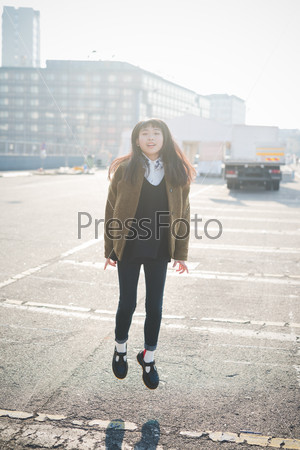 young beautiful asian hipster woman in the city - living town during sunset in backlit jumping and dancing