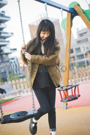 young beautiful asian hipster woman in the city - playing on a swing
