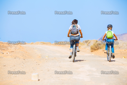 Back view of girl with her mother having a weekend excursion on their bikes on a summer day in beautiful landscape