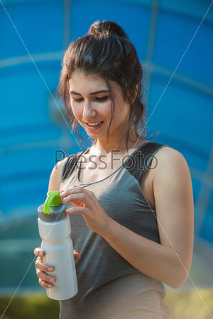Fitness beautiful woman drinking water and sweating after exercising on summer hot day in city. Female athlete after work out.