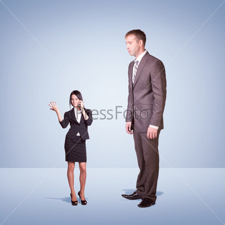 High businessman looking down at little woman using phone. Clouds and cement surface as background. Business concept, stock photo