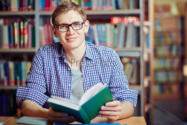 Happy guy sitting in library with interesting book