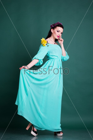 Fashion portrait of pretty teen girl with purple wreath of flowers in hair and fashion makeup is holding daffodil flowers in hands