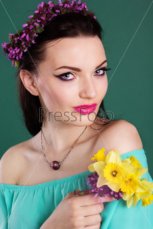 Beauty portrait of pretty girl with purple wreath of flowers in hair and fashion makeup is holding daffodil flowers in hands