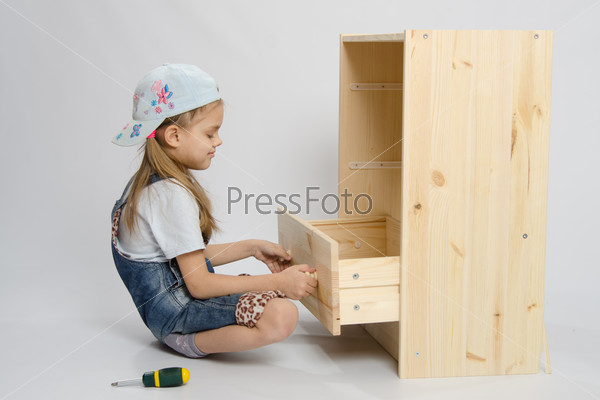 Girl in overalls furniture collector tries to insert drawer a chest of drawers