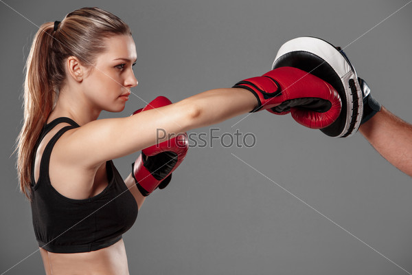 beautiful woman with the red gloves is boxing on gray background