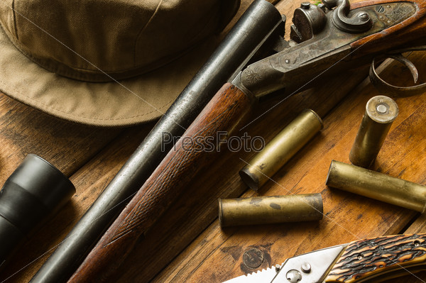 Hunting rifle, ammunition, a knife and a cap on the wooden table, close-up
