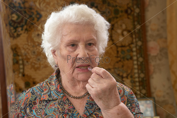 Senior caucasian woman about ninety years old applies lipstick before a three sided mirror in her bed room