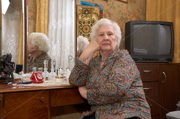 Portrait of senior caucasian woman about ninety years old sitting near the mirror and looking into the camera in her bed room