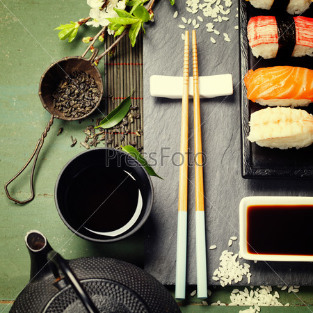 Asian food background (black iron tea set and sushi on rustic table)