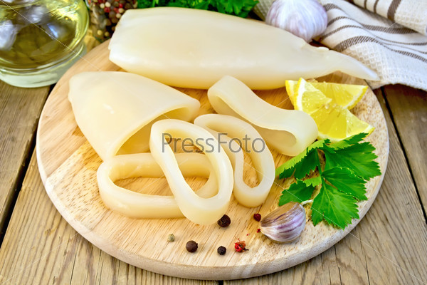 Squid whole and cut into rings, lemon, garlic, pepper, parsley, napkin on wooden board