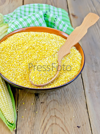 Corn grits in a bowl with a spoon, corn on the cob, napkin on a wooden boards background